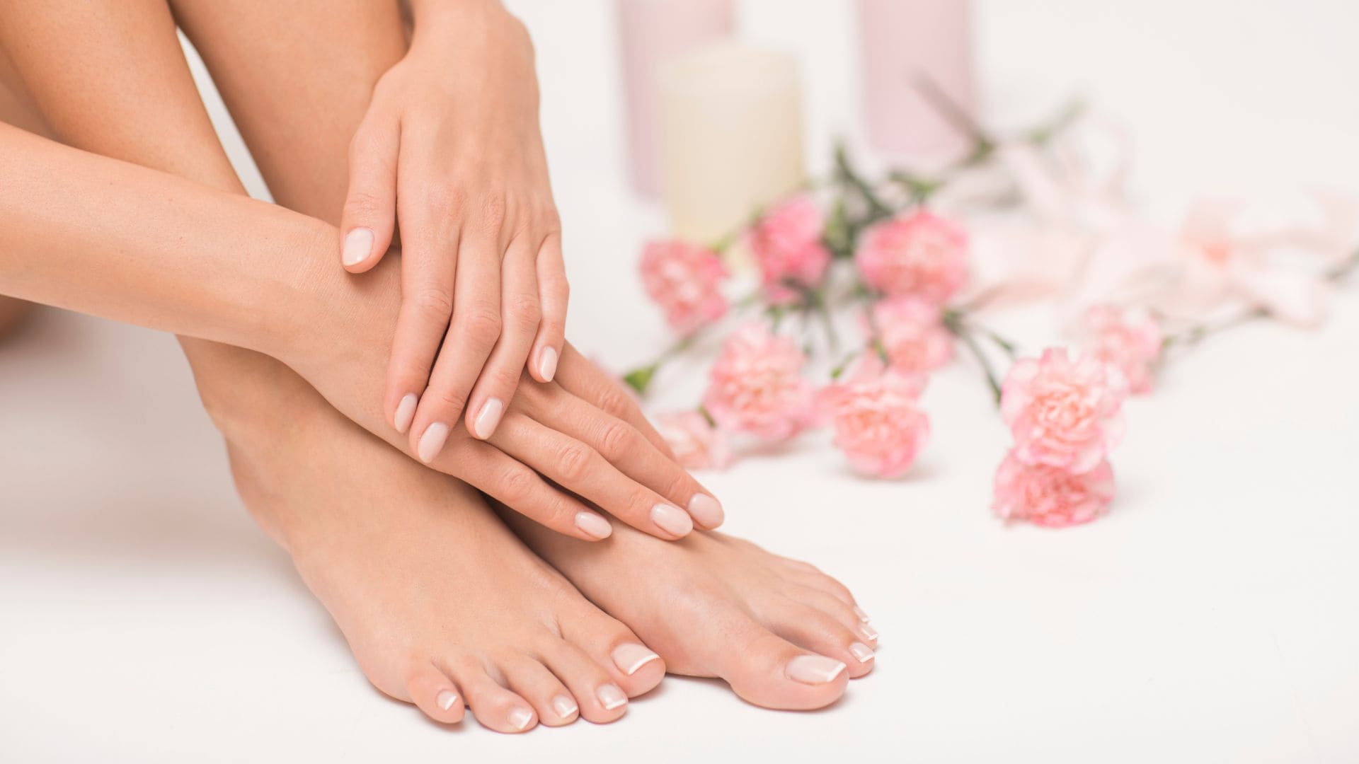 Gepflegte Frauenhände und Füße mit natürlicher Pediküre, umgeben von rosa Blumen. Nahaufnahme für Fußpflege-Kategorie.